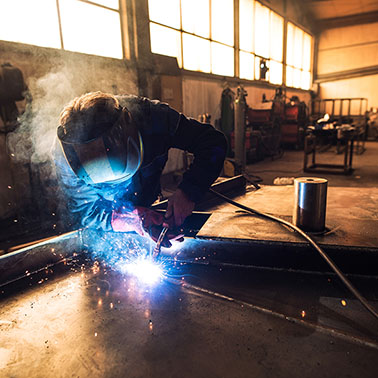 professional welder in protective uniform and helmet welding met
